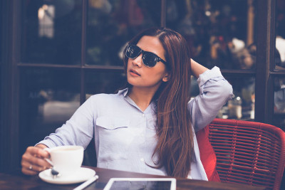 A woman with sunglasses drinking a cup of coffee.